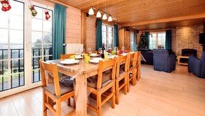 Un intérieur en bois avec une table à manger dressée pour six personnes, une cheminée et un sapin de Noël.