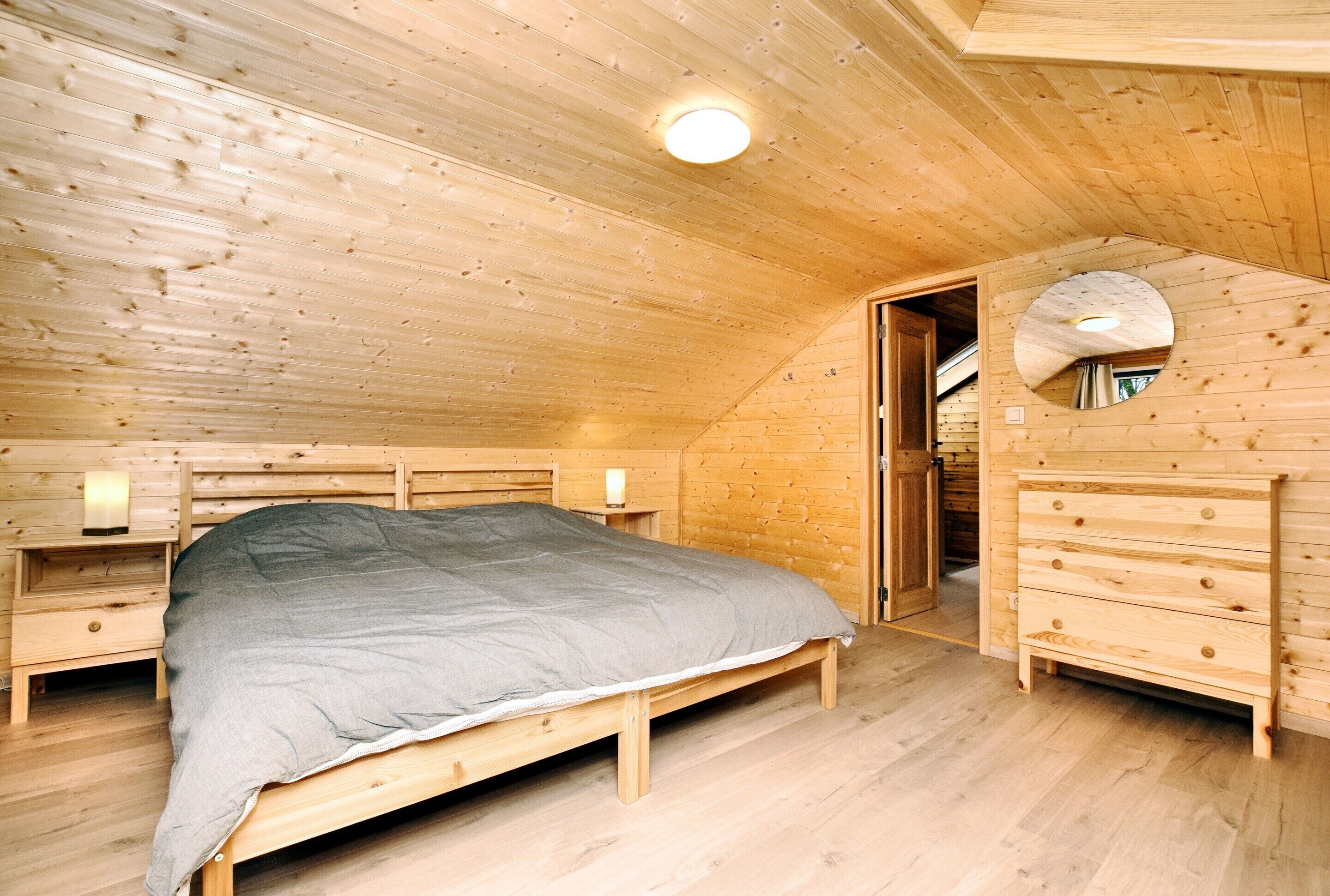 Een houten slaapkamer met een bed, een dressoir en een nachtkastje.