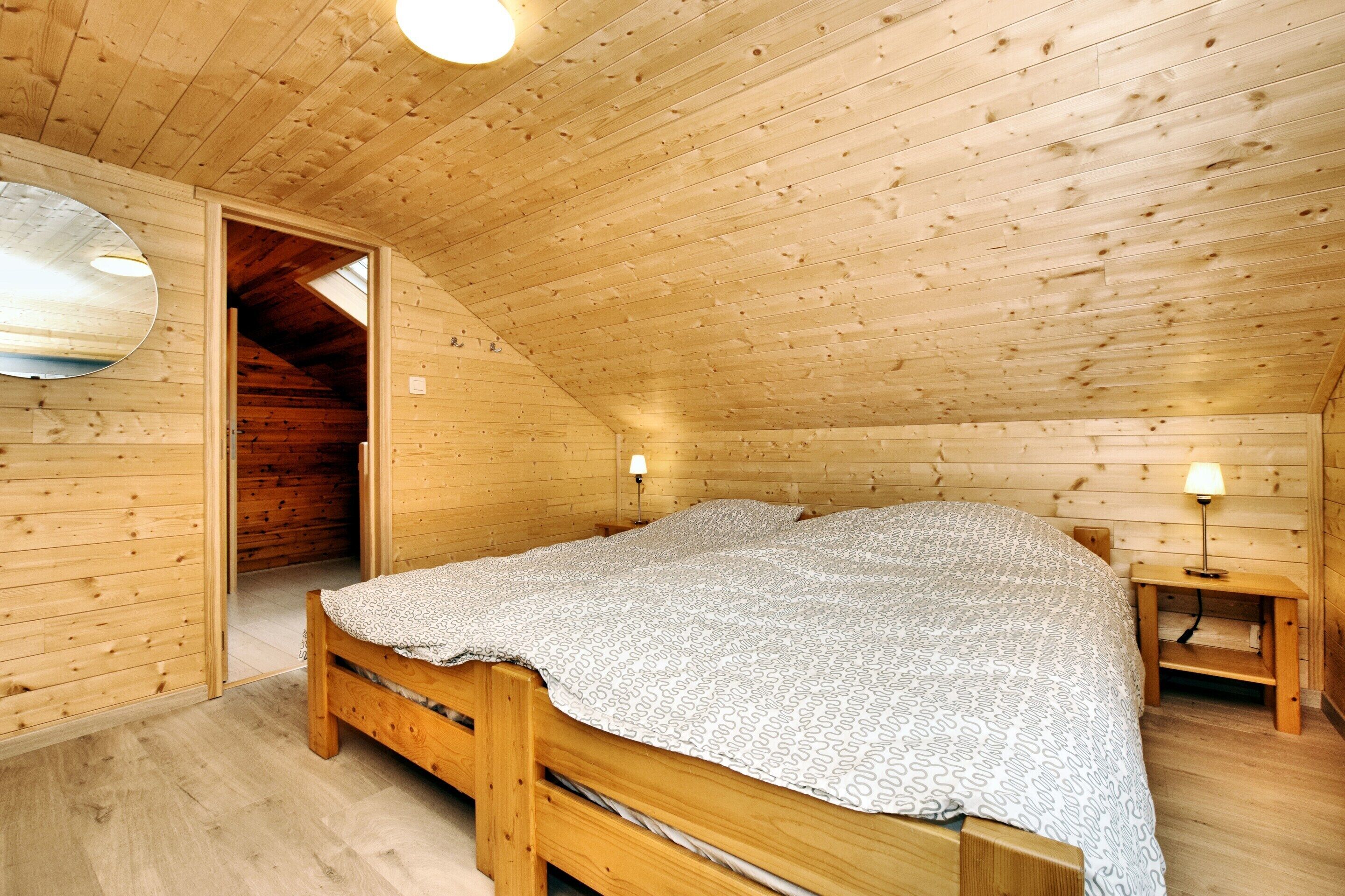 A wooden cabin bedroom with a bed, a nightstand, and a lamp.