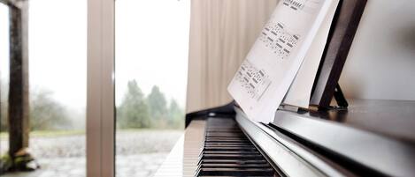 Um piano com partituras em frente a uma janela com vista para árvores e um edifício.