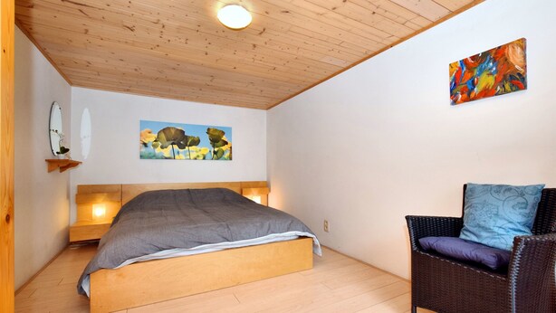 Une chambre à coucher avec un lit en bois, une chaise en osier et un tableau accroché au mur.