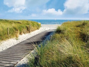 A wooden boardwalk leading to a beach with sand and grassy dunes. - Peaceful Apartment in Zarnewanz near Baltic Sea (Zarnewanz)