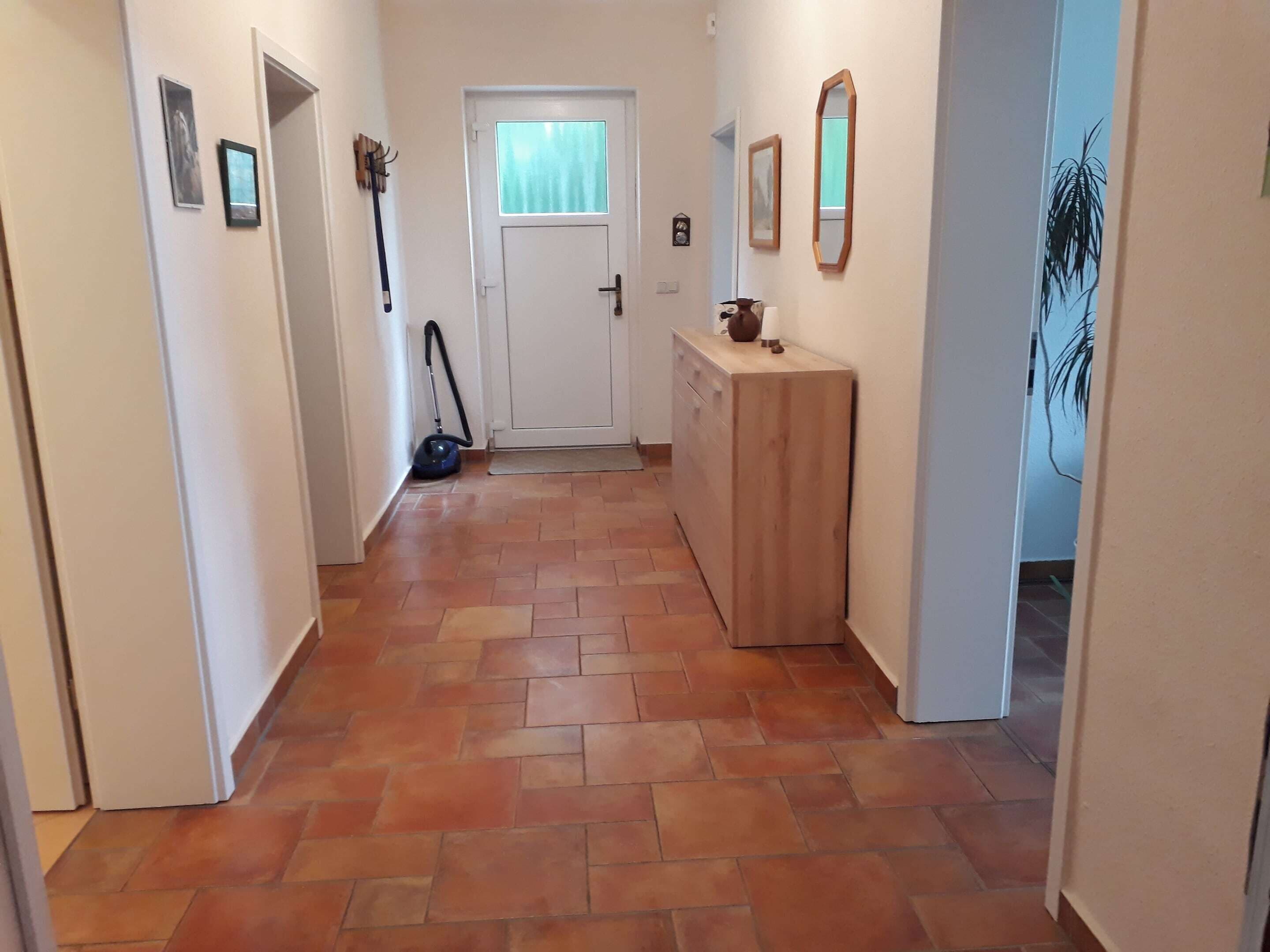 Ein Flur mit Fliesenboden, einer Tür mit Fenster und einem Holzschrank mit Spiegel und einem gerahmten Bild.