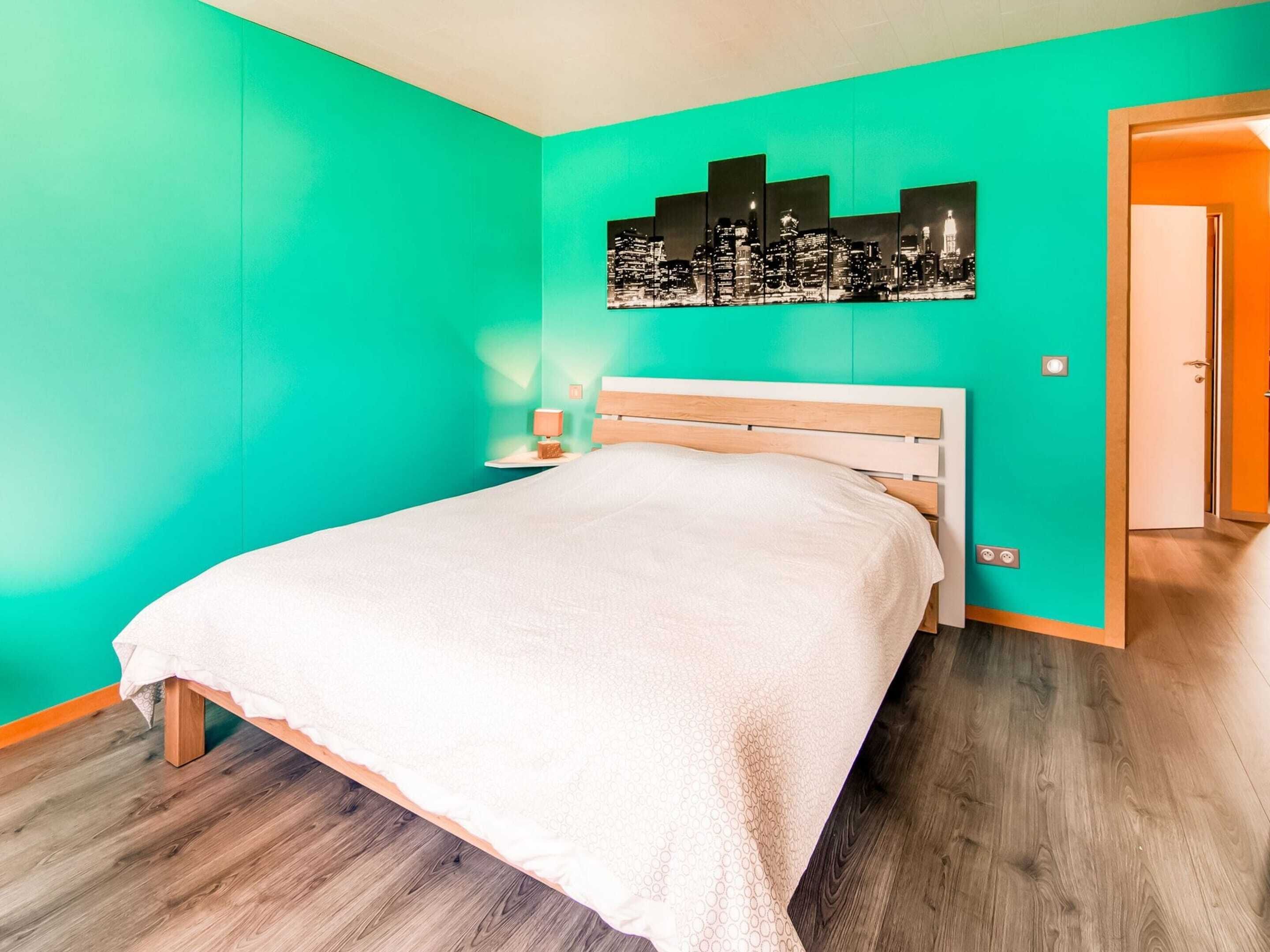 Een slaapkamer met een bed, een nachtkastje, een stadsgezicht kunstwerk aan de muur en een houten deur.