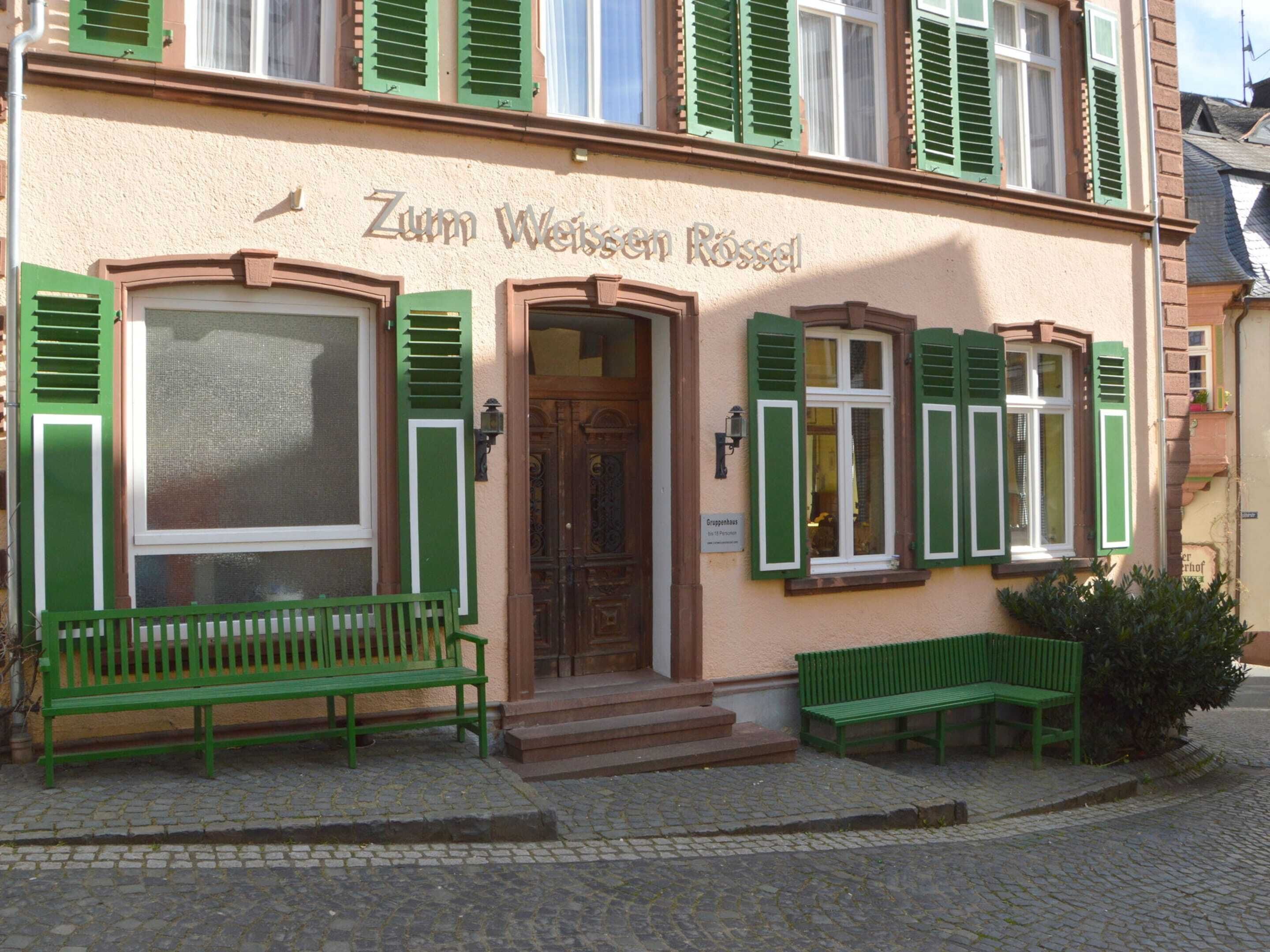 Rakennuksessa on kyltti, jossa lukee ”Zum Weissen Rossel”, ja sen edessä on vihreä penkki.