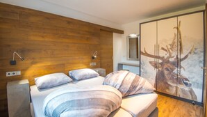 Ein Schlafzimmer mit Holzwand, einem Bett mit gestreifter Bettwäsche, einem Hirschgemälde und einem Nachttisch.
