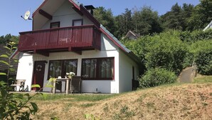 Une maison à deux étages dotée d’un balcon, de grandes fenêtres et d’un petit jardin.