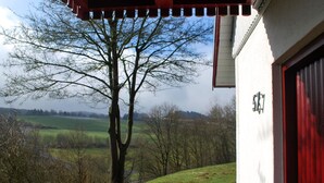 Un bâtiment avec une porte de garage rouge, un arbre devant et, en arrière-plan, une vue sur un champ verdoyant et des arbres.