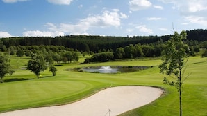 Un parcours de golf doté de bunkers de sable, d’obstacles d’eau et bordé d’une zone boisée.