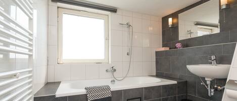A modern bathroom with a large bathtub, a separate sink, and a window providing natural light.