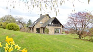 A stone house with a balcony, surrounded by a grassy lawn and trees. - Hillside Retreat With Pond (Lierneux)