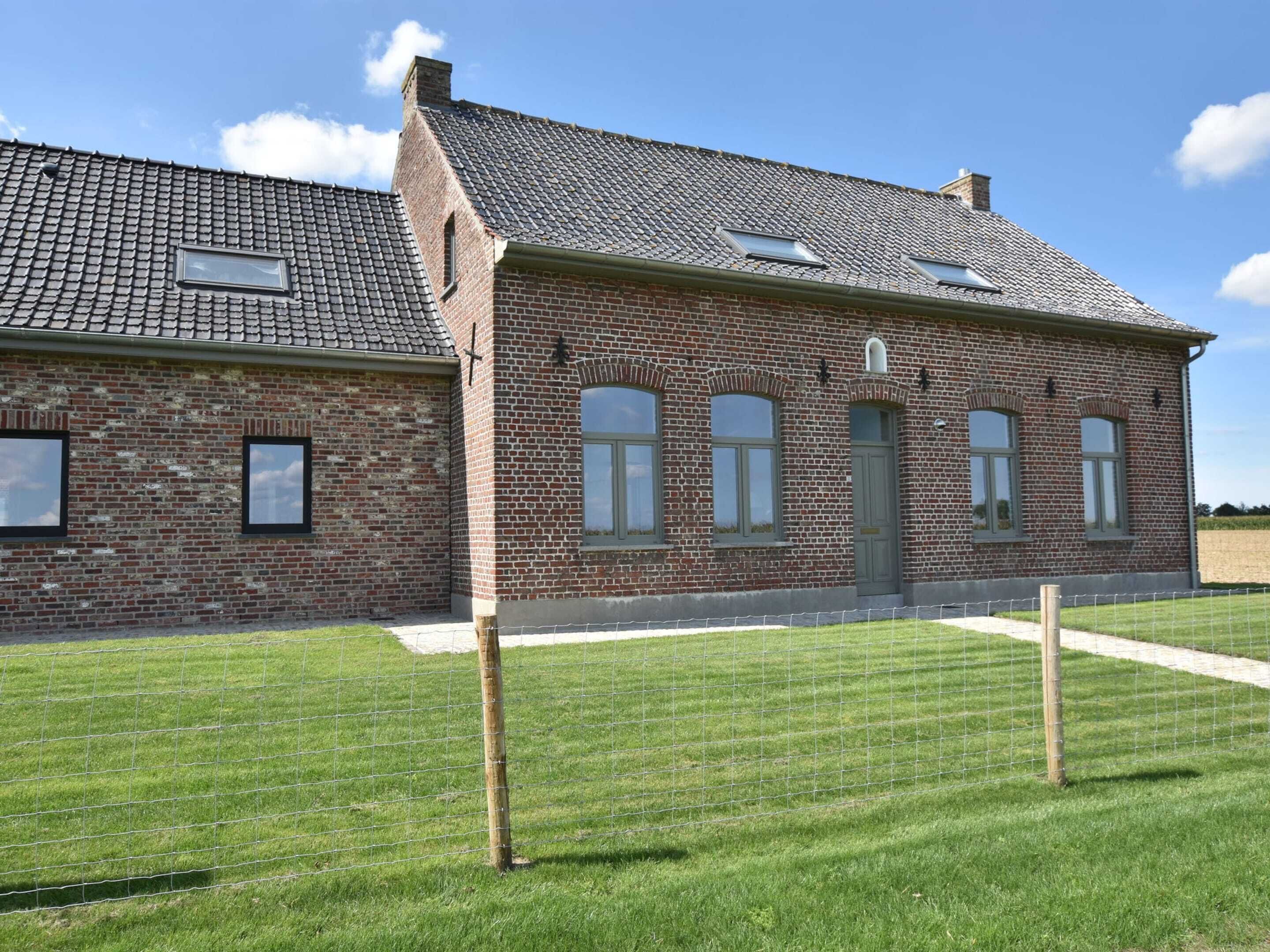 Een gebouw van baksteen met een pannendak, meerdere ramen en een gazon ervoor.
