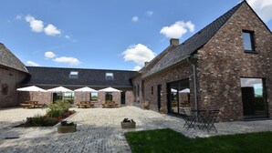 A courtyard with brick buildings, outdoor seating, and umbrellas. - Mansion in Roesbrugge With Garden (Poperinge)