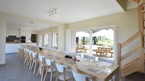 A spacious kitchen with a long dining table and chairs, a staircase, and large windows offering a view of the outdoors. - Mansion in Roesbrugge With Garden (Poperinge)