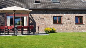 A brick house with a tiled roof, a patio with outdoor furniture, and a small garden with yellow flowers. - Nice Holiday Farmhouse Located in Sourbrodt near Ski Resort of Ovifat (Waimes)