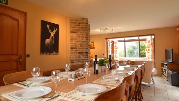 A dining area with a long table set for a meal, a television, and a brick wall. - Nice Holiday Farmhouse Located in Sourbrodt near Ski Resort of Ovifat (Waimes)