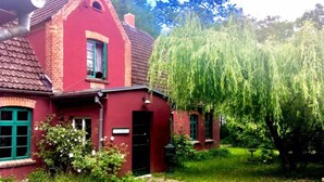 A red brick house with green shutters, a small porch, and a garden with a weeping willow tree. - Wohnung in Neuburg Nahe Ostseestrand (Neuburg)