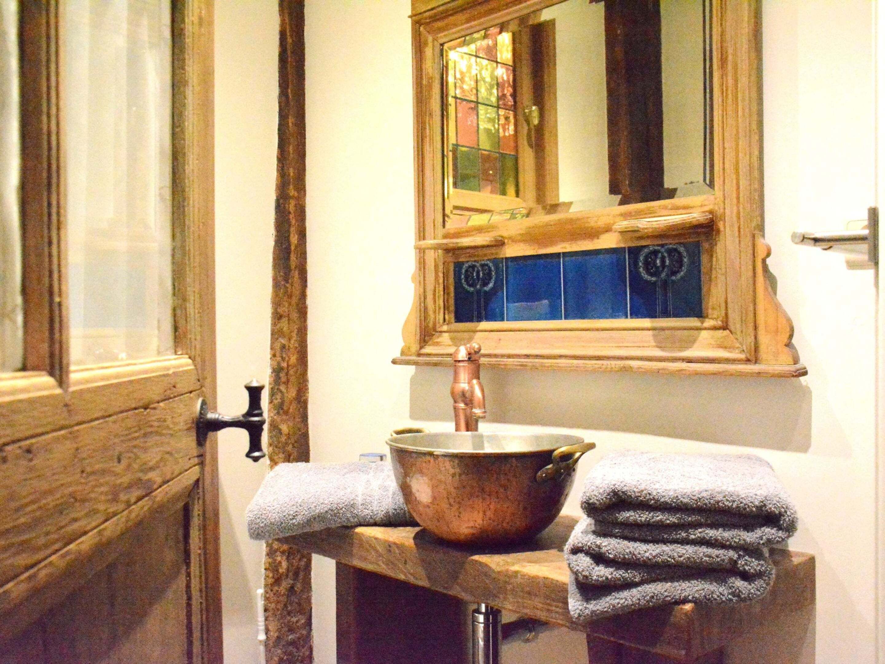 A bathroom with a wooden door, a sink with a copper faucet, a mirror with blue tiles, and a towel rack.