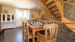 A dining area with a wooden table, chairs, a staircase, and a stone wall. - Sprimont Sauna & Garden Stay (Sprimont)