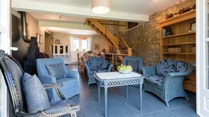 A living room with a fireplace, blue upholstered furniture, a dining area, and a staircase. - Sprimont Sauna & Garden Stay (Sprimont)