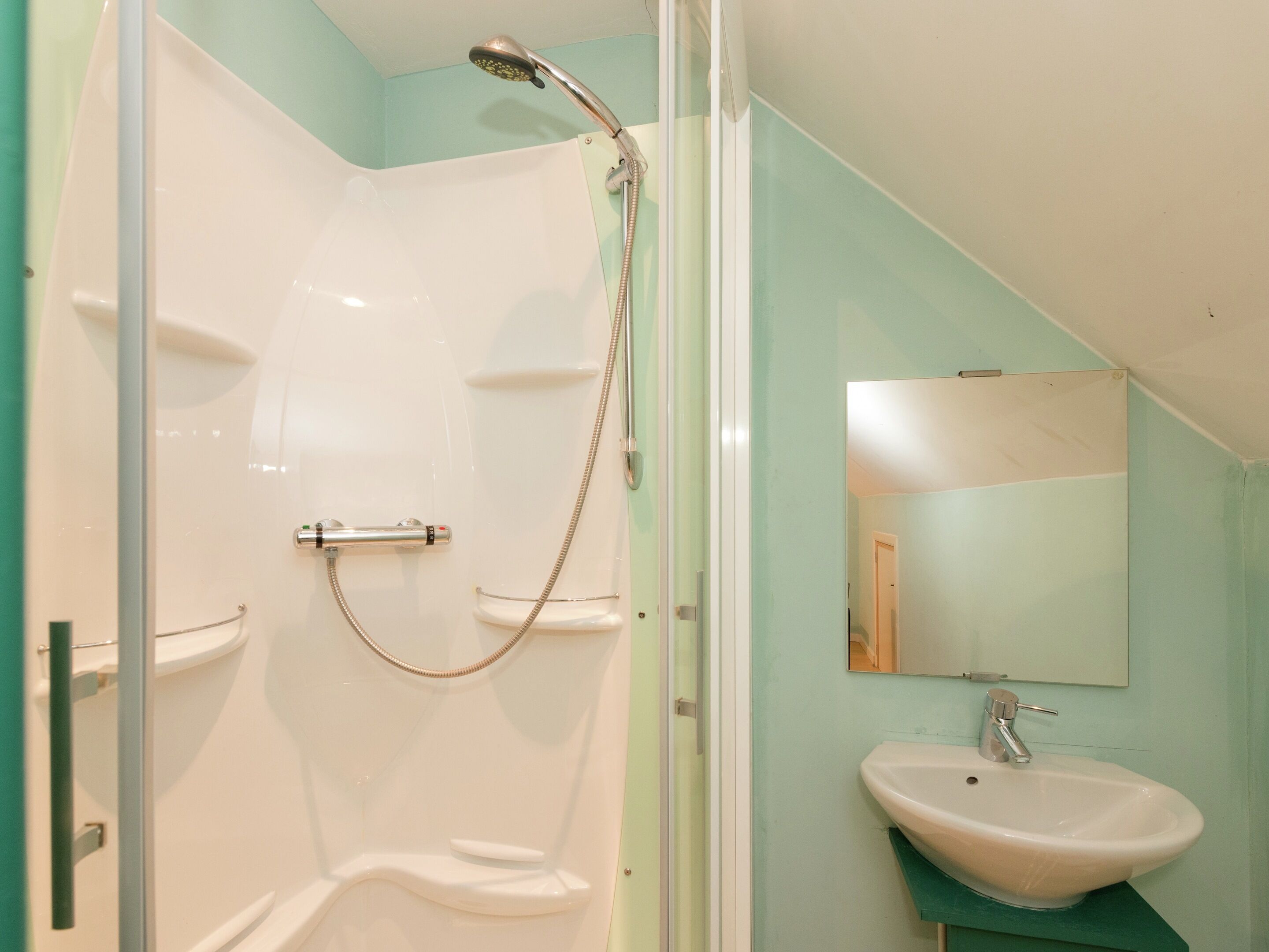 Eine Dusche mit Duschbrause, Glastür und Waschbecken mit Spiegel darüber.
