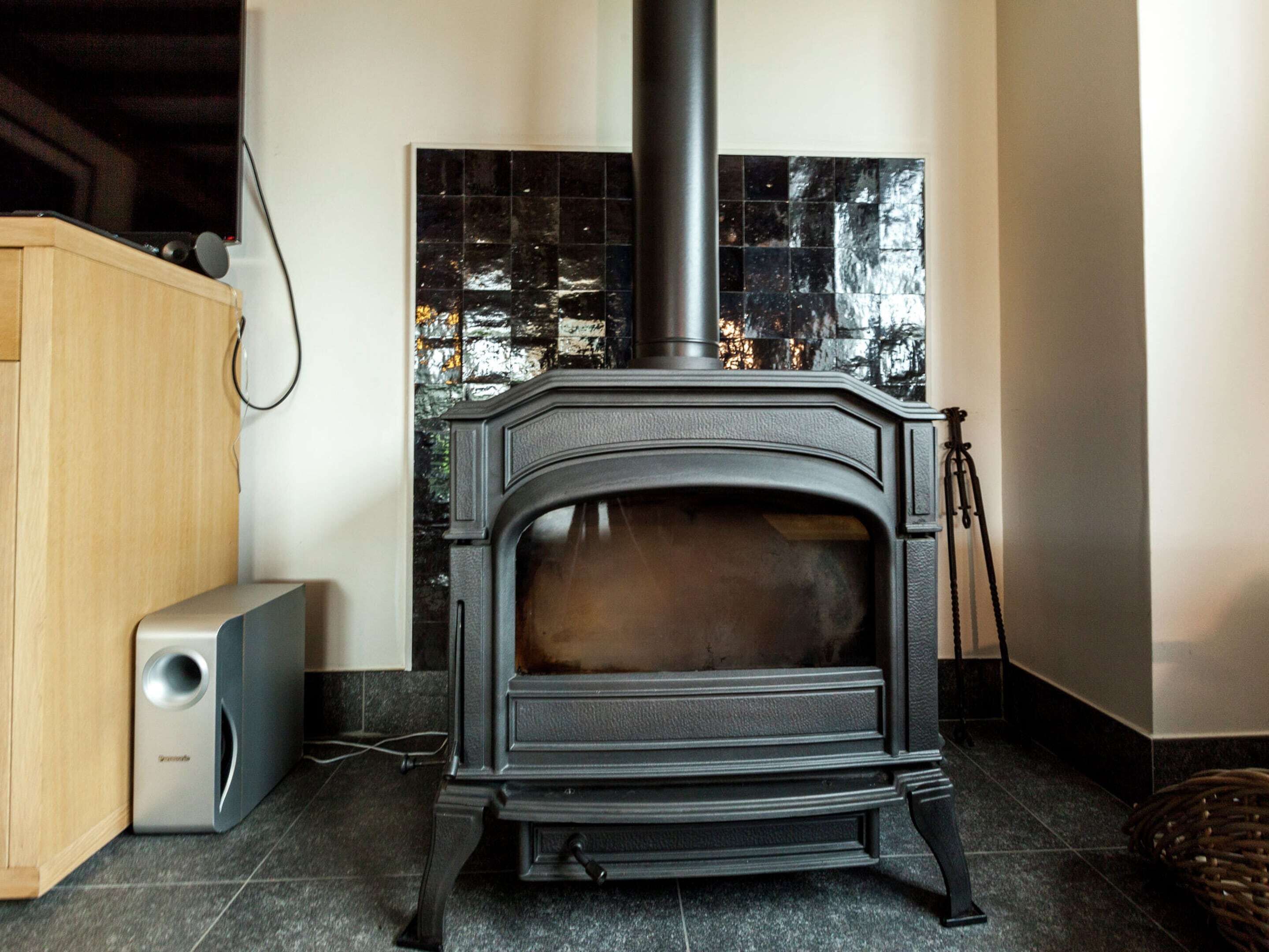 A wood-burning stove with a chimney, a small speaker, and a tiled wall behind it.
