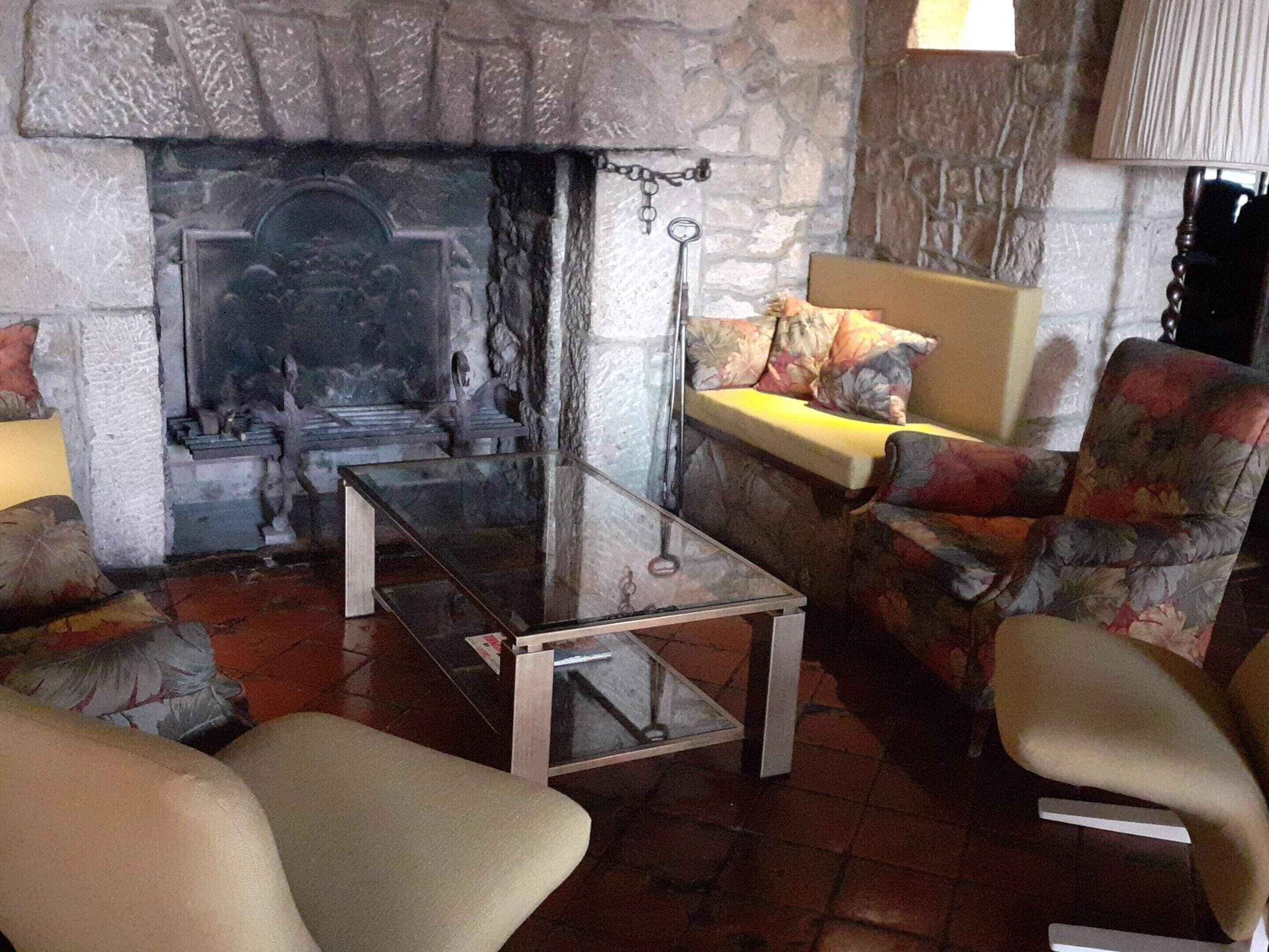 A cozy living room with a stone fireplace, a glass coffee table, and floral-patterned armchairs.