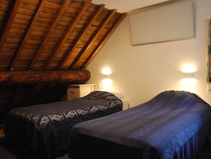 Ein Zimmer mit zwei Betten, einer Holzbalkendecke und zwei Wandleuchten.