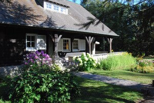 A house with a porch, surrounded by a garden with various plants and flowers.
