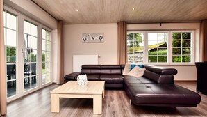 A spacious living room with a large sectional sofa, a wooden coffee table, and a view of a garden through large windows. - Modern Family Home With Wellness (La Roche-en-Ardenne)