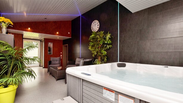 A modern indoor spa area with a hot tub, seating area, and potted plants. - Modern Family Home With Wellness (La Roche-en-Ardenne)