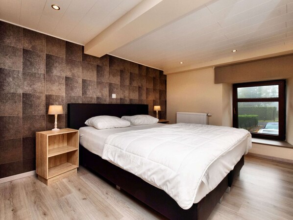 A modern bedroom with a large bed, two bedside tables, a built-in shelf, and a window with a view of the outside.
