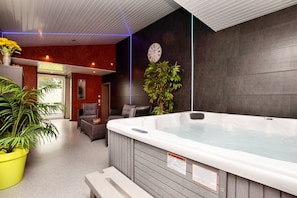A modern indoor spa area with a hot tub, seating, and potted plants.