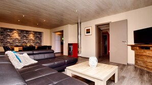 A modern living room with a sectional sofa, a coffee table, a flat-screen TV on a wooden stand, and a stone wall backsplash. - Modern Family Home With Wellness (La Roche-en-Ardenne)