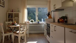 Une cuisine comprenant une table à manger, des chaises, un radiateur, une fenêtre avec des rideaux et des placards.