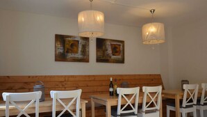 Un espace repas avec des bancs en bois et des chaises blanches, deux tableaux accrochés au mur et des lampes suspendues au-dessus de la table.
