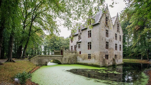 Un bâtiment historique entouré d’arbres, avec un fossé et un pont.
