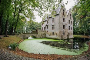 A historic building with a moat and bridge, surrounded by trees.