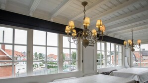 Une chambre d’hôtel avec de grandes fenêtres, un lustre et un lit recouvert d’une courtepointe blanche.