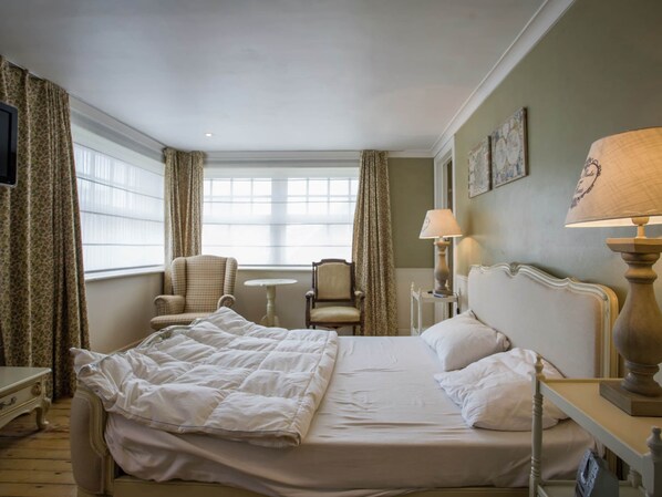 A hotel room with a bed, two armchairs, a small table, and a lamp.