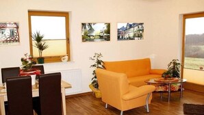 A modern living room with a wooden floor, a dining table with chairs, a sofa, and two windows with pictures on the walls. - Modern Apartment in Morz in the Hunsruck (Buch)