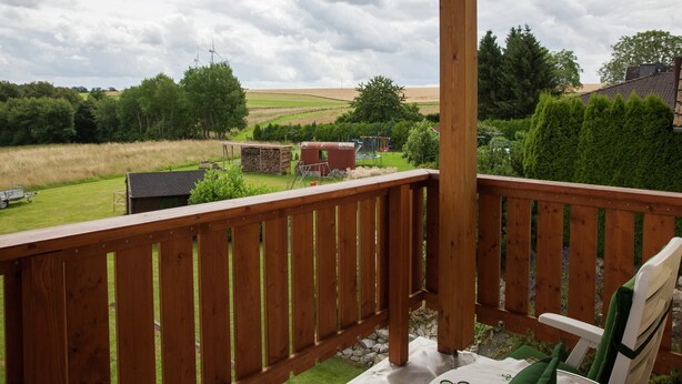 A wooden deck with a view of a rural landscape, including fields, trees, and a distant building. - Modern Apartment in Morz in the Hunsruck (Buch)
