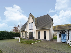 A two-story house with a sloped roof, a small porch, and a sign reading "Jojo Huis."
