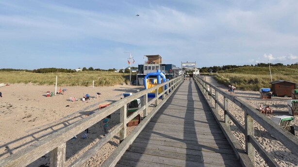 A wooden boardwalk leading to a beach area with a lifeguard station and a sign indicating 'Seebrücke'. - Fewo Ostsee Oldenburg/holstein Garten und Carport (Oldenburg in Holstein)