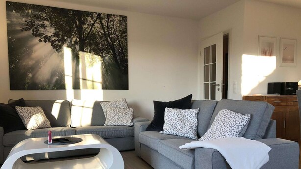A modern living room with grey sofas, patterned cushions, a white coffee table, and a large abstract painting on the wall.