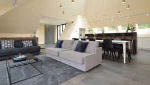 A spacious living area with a grey sofa, a coffee table, and a dining area with a white table and chairs. - Lovely Holiday Home 'walleken' With a Pond (Aalst)