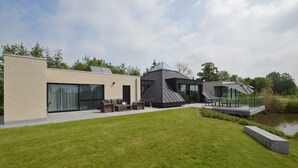 A modern house with a large glass window, a patio with outdoor furniture, and a small pond. - Lovely Holiday Home 'walleken' With a Pond (Aalst)