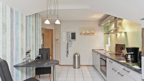 A compact kitchen with a dining area, featuring a modern stove, a coffee maker, and a small trash bin. - Furnished Apartment in Nieheim Germany near Forest (Nieheim)
