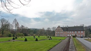 A large, historic building with a symmetrical garden layout, including neatly trimmed hedges and a central fountain. - Furnished Apartment in Nieheim Germany near Forest (Nieheim)