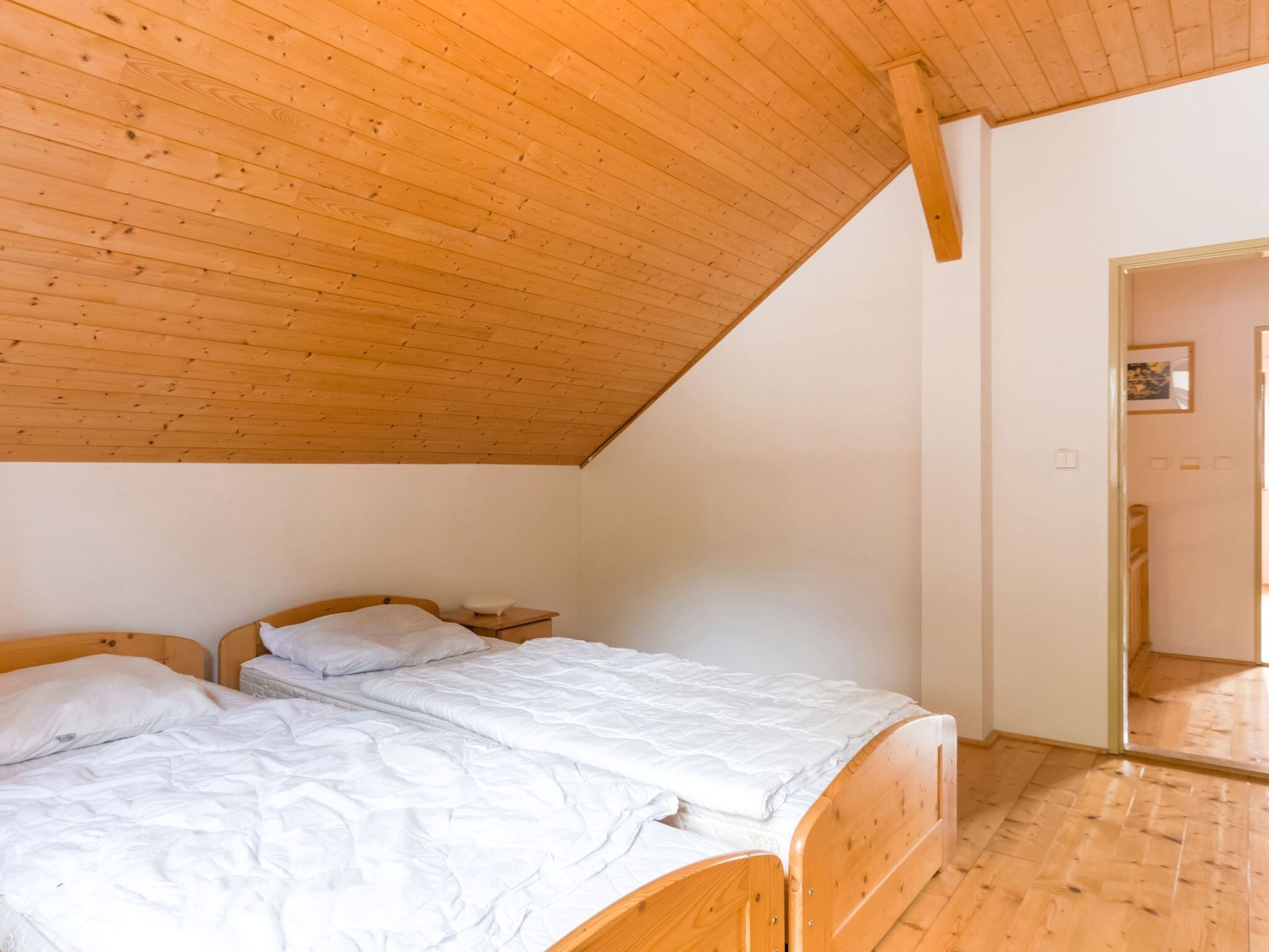 A bedroom with two wooden beds, a sloped ceiling, and a wooden floor.
